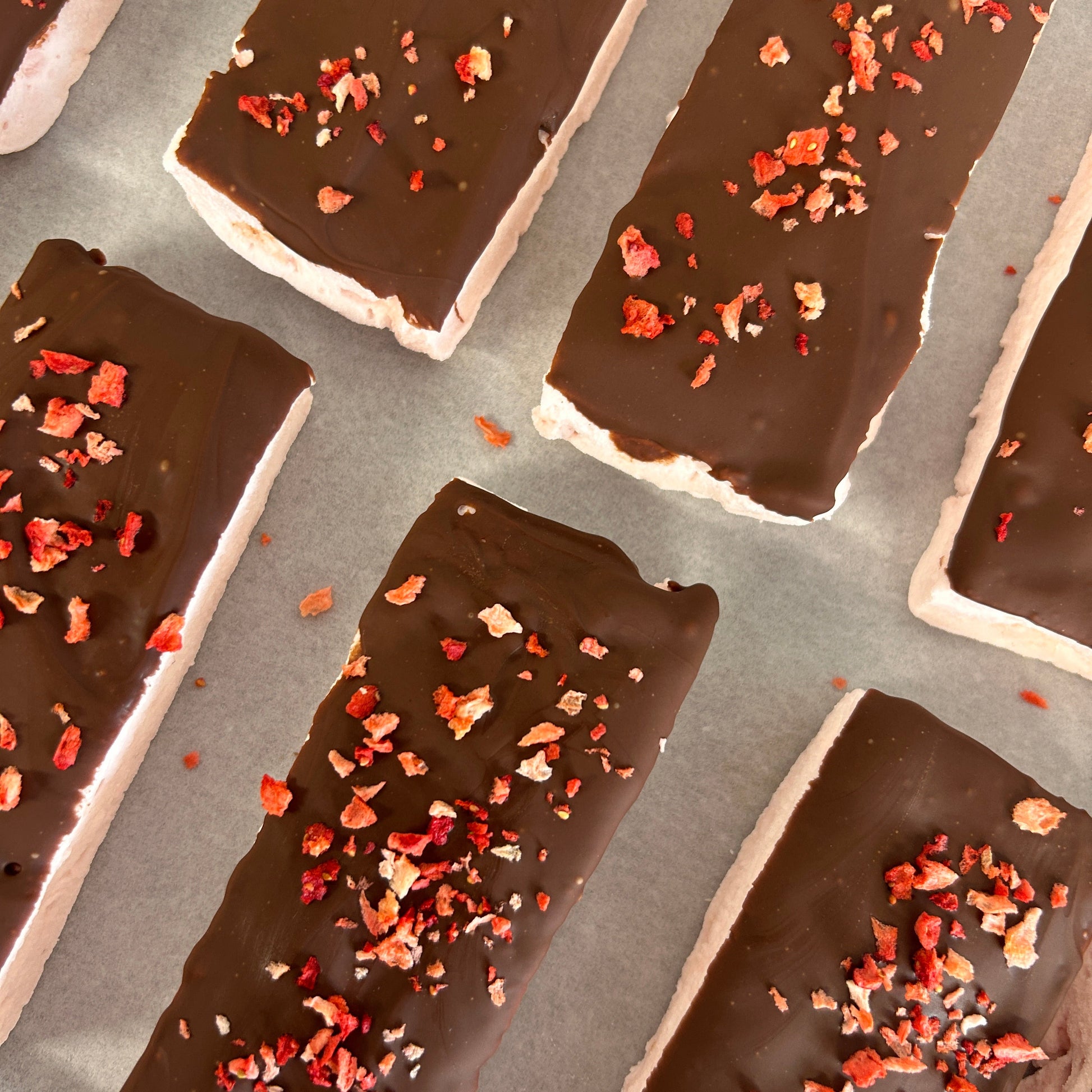 Soft strawberry protein marshmallow coated in creamy milk chocolate and topped with freeze-dried strawberries, handmade in the UK with 9g protein and approximately 160 calories.